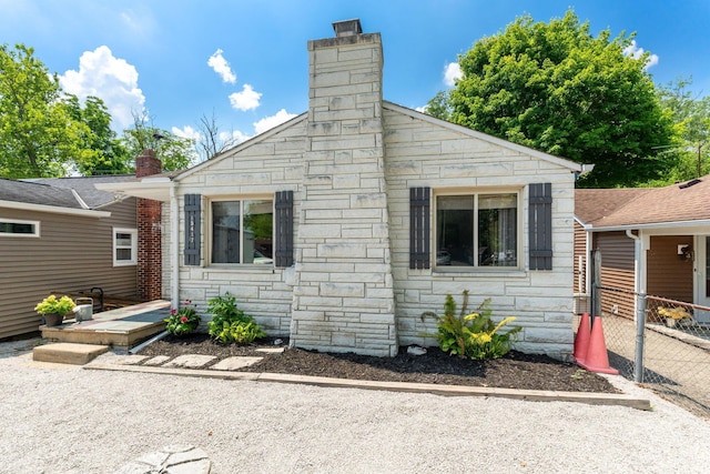 view of side of property with stone siding, a chimney, and fence