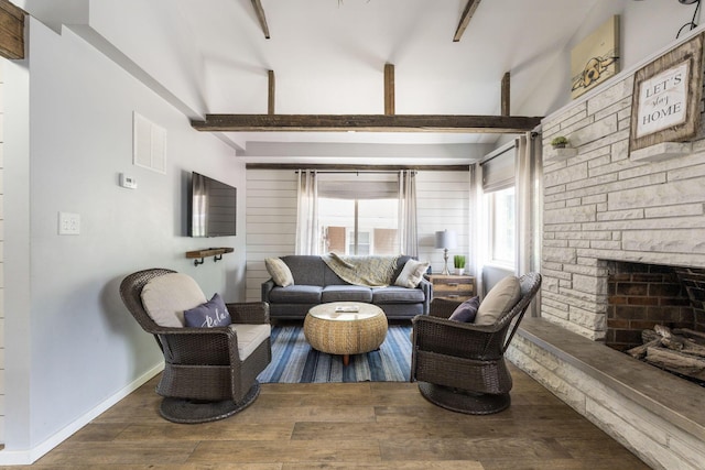 living area with a stone fireplace, wood finished floors, visible vents, baseboards, and beamed ceiling