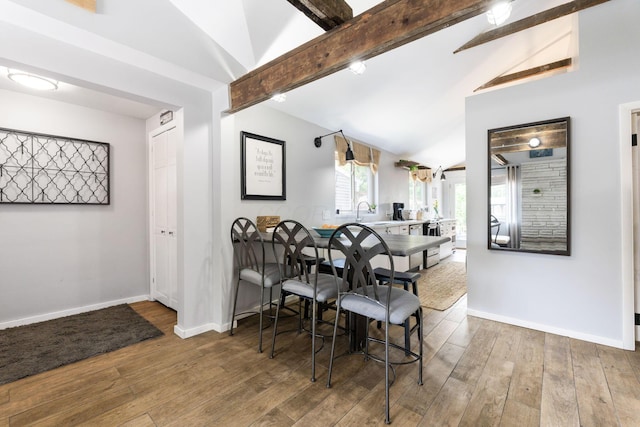 dining space featuring lofted ceiling with beams, wood-type flooring, and baseboards