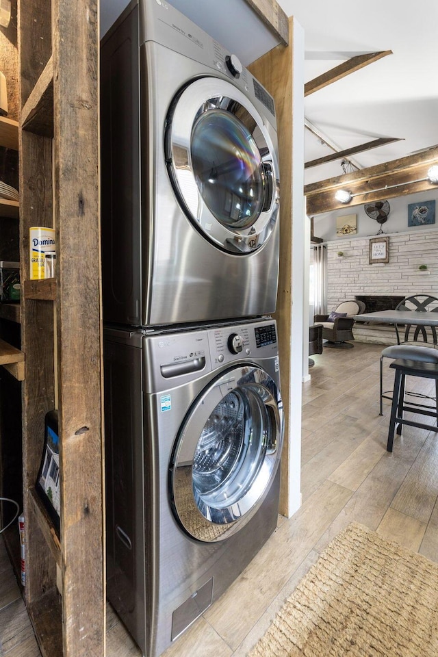 clothes washing area featuring laundry area, stacked washer and dryer, and light wood-style flooring