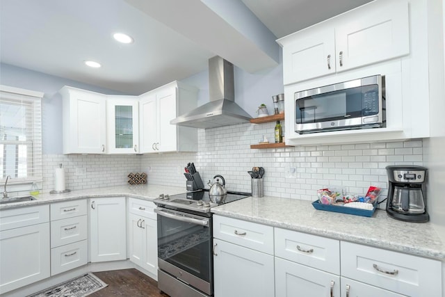 kitchen featuring appliances with stainless steel finishes, white cabinetry, a sink, and wall chimney range hood