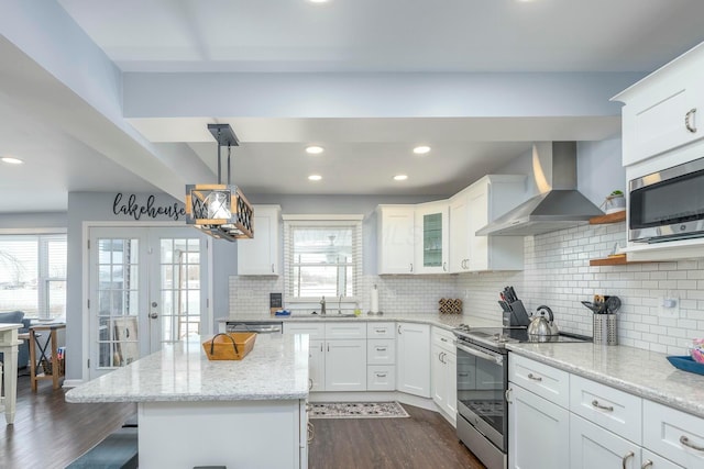 kitchen featuring light stone countertops, white cabinetry, wall chimney range hood, appliances with stainless steel finishes, and a center island