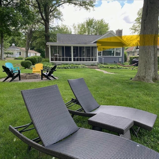 back of property featuring a sunroom, a chimney, a fire pit, and a yard