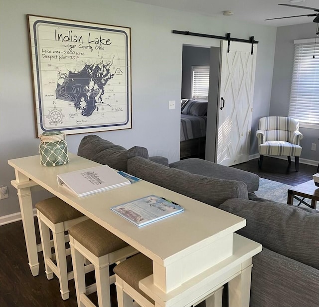 dining space featuring ceiling fan, a barn door, dark wood-type flooring, and baseboards