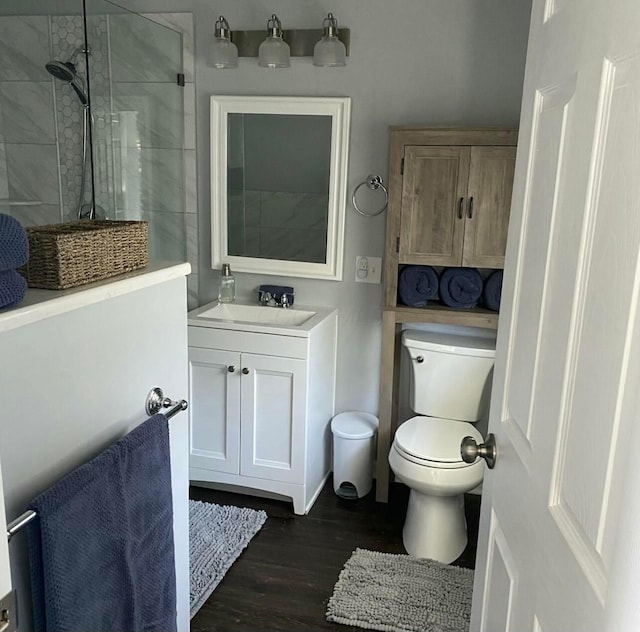 bathroom featuring toilet, wood finished floors, vanity, and a tile shower