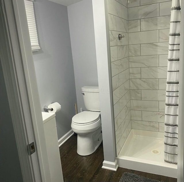 full bathroom with a stall shower, wood finished floors, toilet, and baseboards