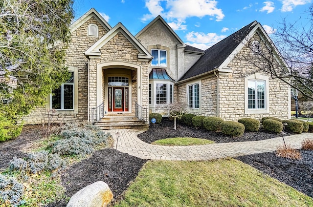 french country style house with a shingled roof and stone siding