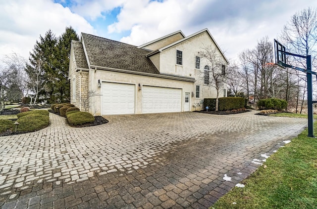 view of home's exterior featuring an attached garage, roof with shingles, decorative driveway, and stucco siding