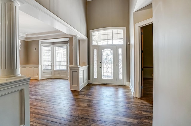 foyer entrance with a decorative wall, dark wood-style flooring, wainscoting, ornate columns, and crown molding