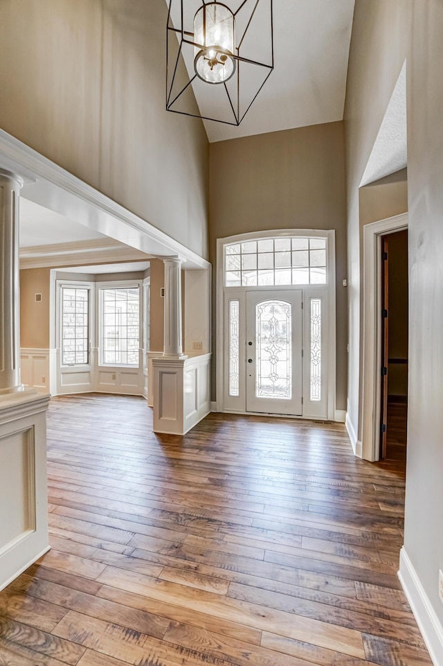 foyer entrance featuring hardwood / wood-style flooring, a decorative wall, a high ceiling, ornate columns, and an inviting chandelier