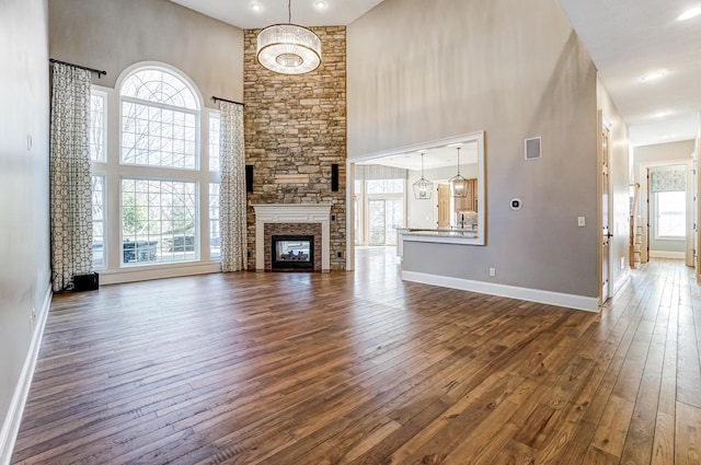 unfurnished living room featuring baseboards, visible vents, dark wood-style floors, a high ceiling, and a fireplace