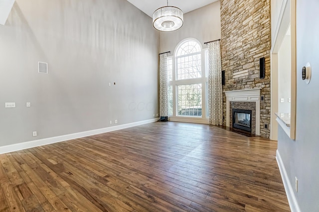 unfurnished living room featuring dark wood-style floors, a stone fireplace, a high ceiling, and baseboards