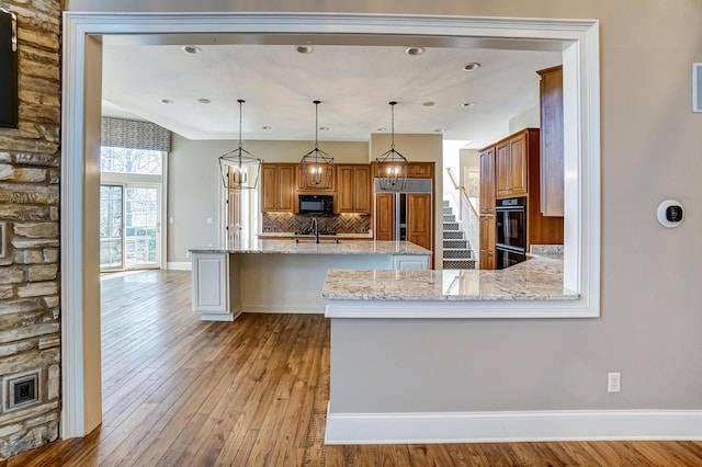 kitchen with light wood finished floors, decorative backsplash, brown cabinetry, light stone counters, and black appliances