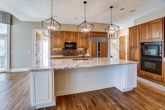 kitchen featuring black appliances, a sink, a large island with sink, and brown cabinets