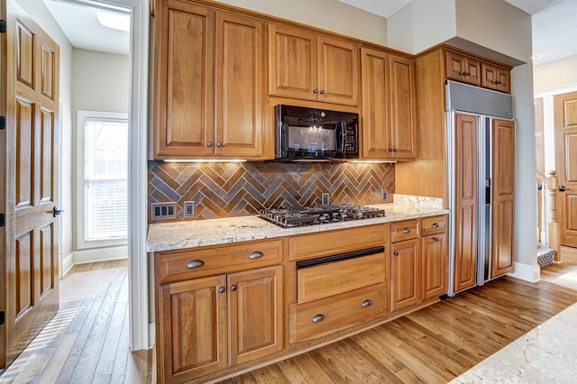 kitchen with paneled built in fridge, black microwave, light stone counters, light wood-style floors, and stainless steel gas cooktop