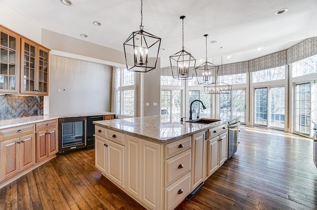 kitchen featuring pendant lighting, glass insert cabinets, a kitchen island with sink, a sink, and beverage cooler