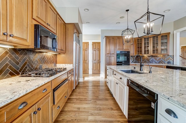 kitchen with a sink, white cabinetry, light stone countertops, black appliances, and glass insert cabinets