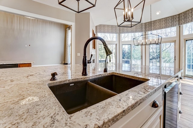 room details with an inviting chandelier, a sink, decorative light fixtures, and light stone countertops