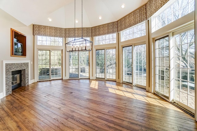 unfurnished living room with a notable chandelier, light wood-style floors, a stone fireplace, high vaulted ceiling, and baseboards