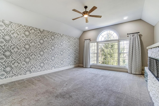 unfurnished living room featuring light carpet, baseboards, ceiling fan, vaulted ceiling, and a fireplace