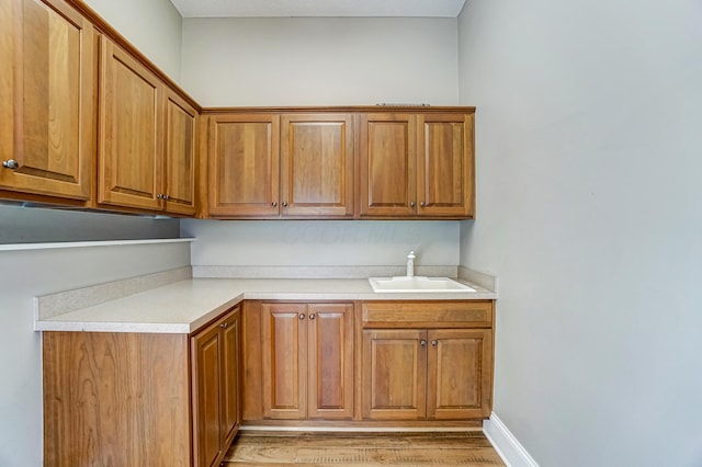 kitchen featuring a sink, baseboards, light wood-style floors, light countertops, and brown cabinetry