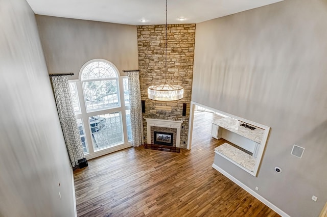 unfurnished living room featuring a towering ceiling, wood finished floors, and a stone fireplace