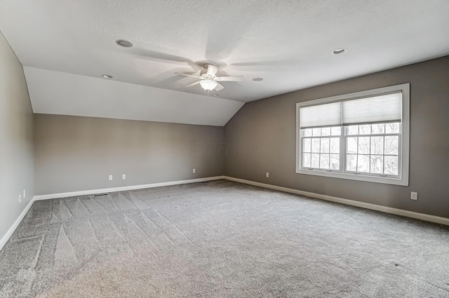 additional living space with carpet, vaulted ceiling, a textured ceiling, ceiling fan, and baseboards