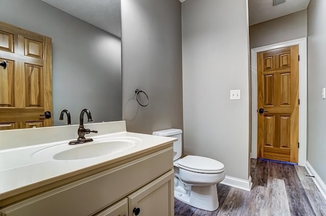 bathroom featuring toilet, baseboards, wood finished floors, and vanity