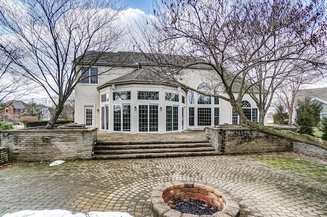 rear view of property featuring a patio, an outdoor fire pit, and stucco siding