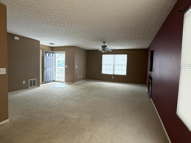 unfurnished room featuring a textured ceiling, light carpet, a ceiling fan, visible vents, and baseboards