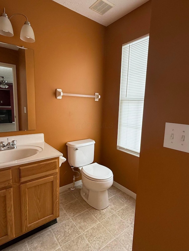 half bathroom with toilet, vanity, visible vents, and baseboards