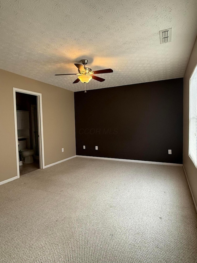 carpeted spare room featuring visible vents, ceiling fan, a textured ceiling, and baseboards