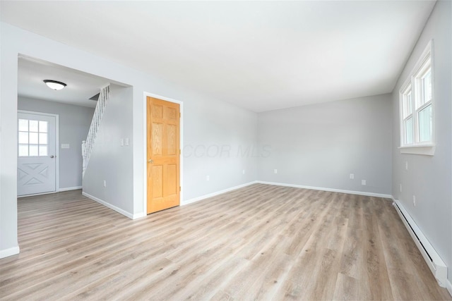 unfurnished room with a baseboard heating unit, stairway, light wood-type flooring, and baseboards