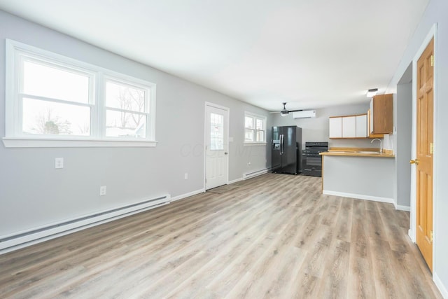 unfurnished living room with ceiling fan, a baseboard radiator, a sink, baseboards, and light wood-style floors