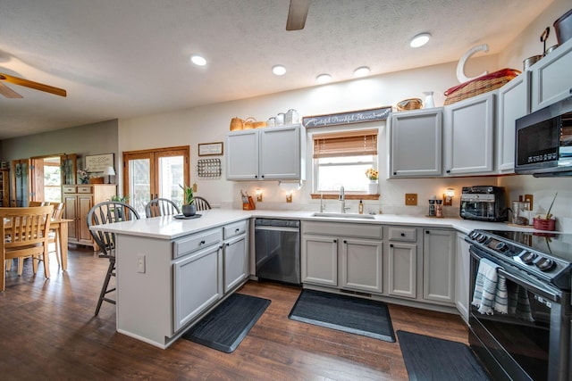 kitchen featuring a peninsula, stainless steel appliances, a sink, light countertops, and a kitchen bar