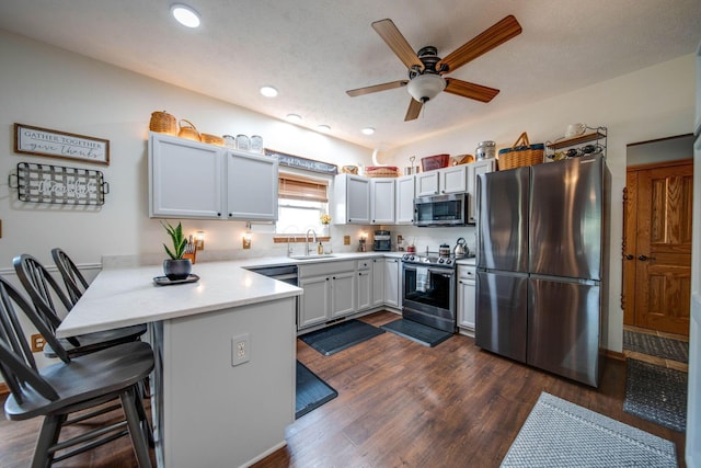 kitchen with a kitchen breakfast bar, a peninsula, stainless steel appliances, white cabinetry, and a sink