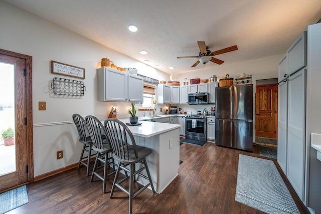 kitchen with a peninsula, a breakfast bar, a sink, light countertops, and appliances with stainless steel finishes