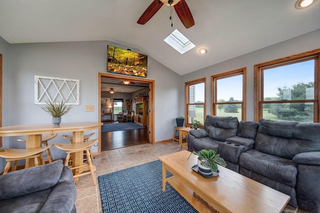 living room with lofted ceiling with skylight, light tile patterned floors, baseboards, and a ceiling fan