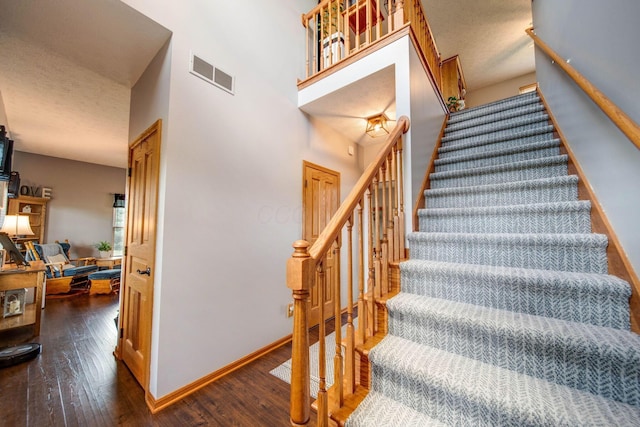 stairs featuring hardwood / wood-style flooring, a towering ceiling, visible vents, and baseboards