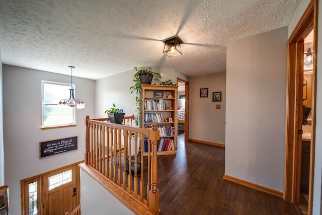 hall with baseboards, dark wood-style floors, an inviting chandelier, a textured ceiling, and an upstairs landing