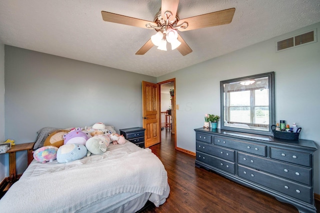 bedroom featuring ceiling fan, visible vents, dark wood finished floors, and a textured ceiling