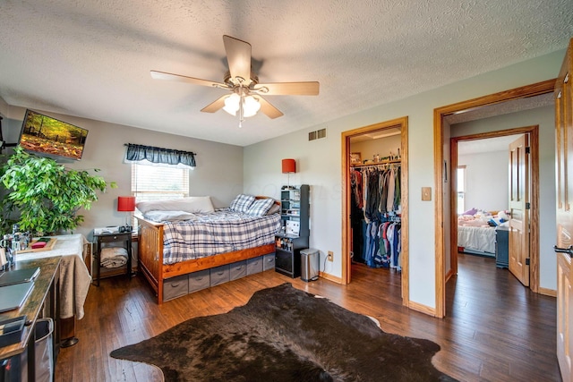 bedroom featuring baseboards, visible vents, dark wood-type flooring, a spacious closet, and a textured ceiling