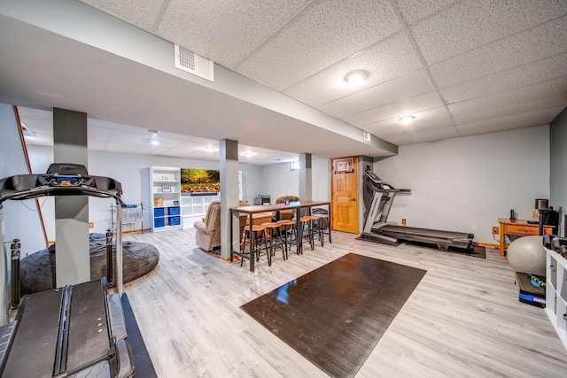 exercise area with light wood-type flooring, visible vents, and a drop ceiling