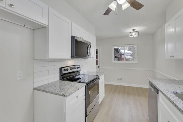 kitchen with stainless steel appliances, backsplash, white cabinetry, and light stone countertops