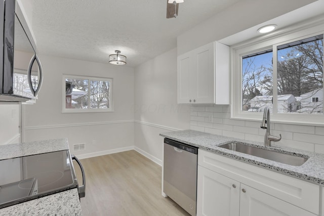 kitchen with range with electric stovetop, stainless steel dishwasher, white cabinets, a sink, and light stone countertops