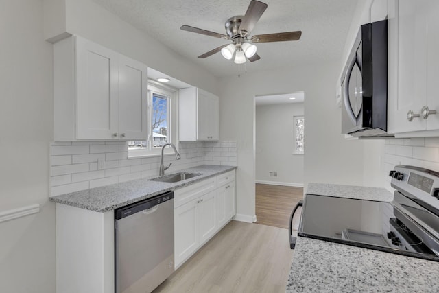 kitchen featuring appliances with stainless steel finishes, white cabinets, a sink, and light stone counters