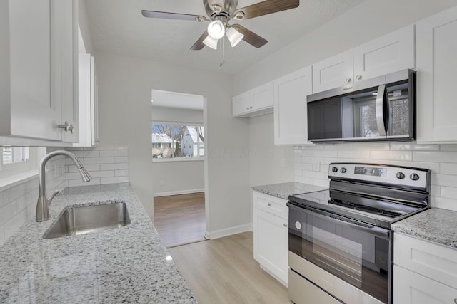 kitchen with appliances with stainless steel finishes, white cabinets, a sink, and light stone counters