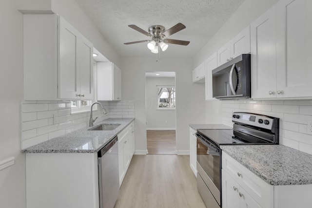 kitchen featuring white cabinetry, appliances with stainless steel finishes, light stone counters, and a sink