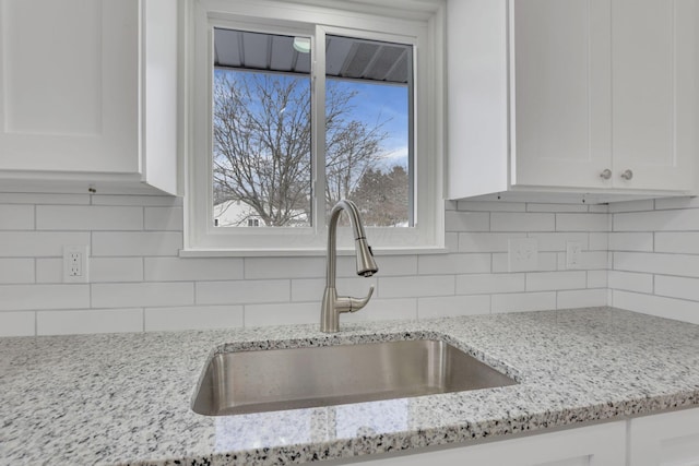 kitchen with light stone counters, white cabinetry, a sink, and tasteful backsplash