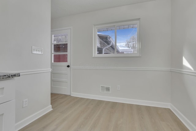 empty room featuring light wood-style floors, visible vents, a textured ceiling, and baseboards